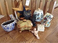 Collection of various decorative items on wooden table including ceramic jars, a trinket box, a cherub figurine, and a planter.