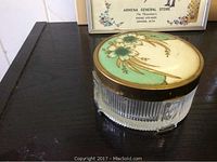 Photo showing the top view of the vintage powder dish with floral lid featuring blue flowers and green background.