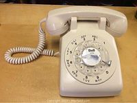 Front view of the cream Bell rotary telephone showing circular numbered dial and coiled cord.