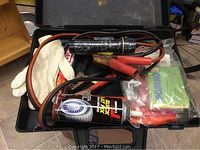 Top view of the open black carrying case showing contents including jumper cables, gloves, and tire repair spray.