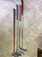 Four golf putters laid on tile floor showing grip colors and shafts.