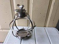Full view of the metal candle carrier showing its spherical cage frame, ring handle, and flat base.