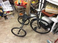 Full view of tricycle showing frame, three spoked wheels, and metal saddle seat.