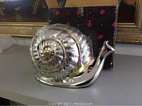 Photo showing metal snail storage container with shell lid on, next to box.