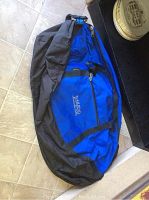 Full view of large blue and black Trailhead duffel bag lying on floor, showing zipper and logo.