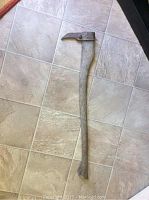 Full view of the antique pick axe tool showing wooden handle and metal head lying on tile floor.