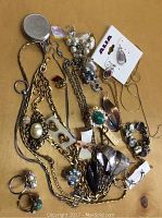 Mixed assortment of jewelry laid out showing various necklaces, brooches, rings, earrings, and a bracelet with tangle corrected.