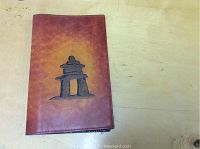Photo showing front view of the brown leather book cover with black inuksuk design placed on a wooden surface.