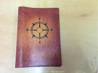Top view of brown leather book cover with black compass rose design on front, placed on a light wood surface.