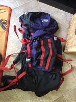 Front view of the hiking backpack showing blue and black fabric with red straps and multiple side pockets.