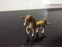 Solid brass unicorn figurine with raised front leg and spiral horn on a dark surface.