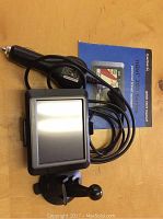 Garmin Nuvi 205 GPS device with attached charger cable and quick start manual laid on wood surface.