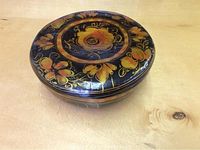 Large round lidded bowl with intricate painted floral design on black surface, showing the top lid.