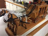 Front and side view of the full wooden stagecoach with horses mounted on a wooden base, showing the smooth finish and detailed ribbons on horses.
