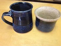 Photo showing dark blue glazed pottery mug with handle and matching smaller cup with tan interior, both handmade