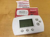 White Honeywell programmable thermostat with display screen and buttons, shown with operating manual.