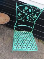 Turquoise metal garden chair with lattice seat and butterfly leaf design on backrest, viewed from slightly above showing seat and foot legs.