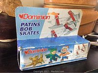 Photo of vintage Dominion bob skates in original packaging box with winter scene illustration and red straps visible on product.