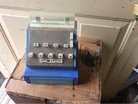 Vintage Tom Thumb cash register toy in blue with white and silver detailing, front view showing buttons and brand name.
