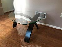 Side view of round glass top cocktail table with curved wood base and stainless steel connectors