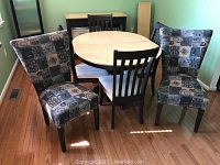 Dining room set with oval wooden table, six chairs including two patterned accent chairs, and four black chairs with white seats on wooden floor.