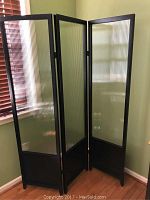 Three-panel folding room partition with textured glass and wood frame shown standing in a room corner with hardwood floor.