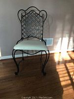 Metal frame chair with lattice backrest and light upholstered cushion with stains on wooden floor and beige wall background