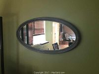 Oval wall mirror mounted on a wall, showing size and frame detail.