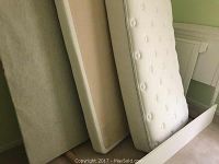 White framed child's bed components including mattress, boxspring, and platform leaning against the wall.