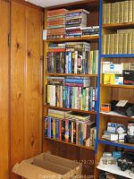 Four wooden shelves filled with vintage science fiction books, showing a mix of hardcover and paperback editions in various colors stacked vertically and horizontally.