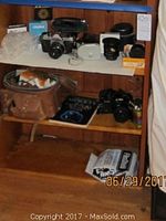 Full view of shelf with Pentax Asahi K1000 camera, Minolta X-700 camera, lenses, brown leather camera case, and accessories.