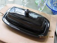 Photo of black Fiesta butter dish with lid placed on its tray, sitting on a cardboard surface.