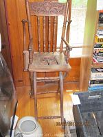Vintage wooden high chair with carved backrest and damaged cane seat shown front view
