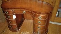 Full view of kidney-shaped wooden desk with multiple drawers and brass ring pull handles, showing general condition.