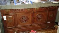 Front view of vintage wooden credenza showing carved floral panels, drawers, and wear on surface.