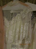 Photo showing the lace detailing and sheer fabric of the white Victorian style wedding dress alongside part of the pink silk-type bed jacket.