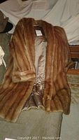 Muskrat fur coat displayed on chair showing brown fur and satin lining.