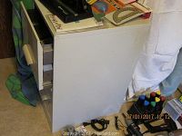 White 2-drawer file cabinet positioned with drawers partly open, showing signs of rust on top surface and surrounding office supplies placed on top and around it.