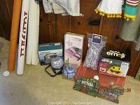 Photo showing Chia Pet emoji new in package, wooden painted blocks depicting Connecticut buildings, Grundig emergency radio, Dorcy light, lavender insert, drawer organizers, candle, and plastic storage container with handles on carpeted floor against wood panel wall.