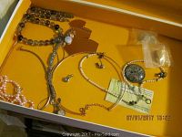 Photo of box showing assorted necklace chains, earrings, and pendants including a pearl necklace and silver floral pendant.