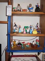 Overall view of wooden shelves displaying multiple small McDonald's Disney Happy Meal figures from the 1990s. Top shelf has Snow White with dwarfs, middle shelf Beauty and the Beast figures, bottom shelf Little Mermaid characters.