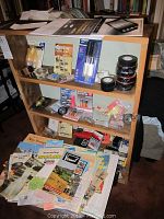 Wooden bookcase filled with electrical tape, battery testers, plumbing parts, hardware accessories, and travel brochures in foreground (brochures not included).