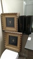 Two custom framed Fleur de Lis prints and two tall black metal Fleur de Lis vases displayed together.