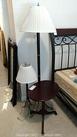 Photo of floor lamp, table lamp on oval table next to bed frame.