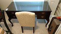 Desk with removable glass top and upholstered chair positioned in front, showing general shape and style.
