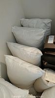 Several white standard size pillows stacked against a wall, some used as decorative shams