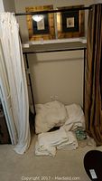 Lot shown with drapes hanging on metal rack, white bedding folded on floor nearby.
