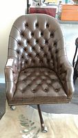 Full front view of the brown leather vintage office chair showing button tufting and studded trim along base.