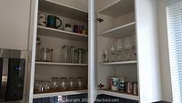 Cupboards with various drinking glasses, jars, and stemware arranged on shelves.