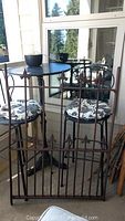 Full view of the vintage wrought iron gate standing upright near patio furniture, showing overall design and size.